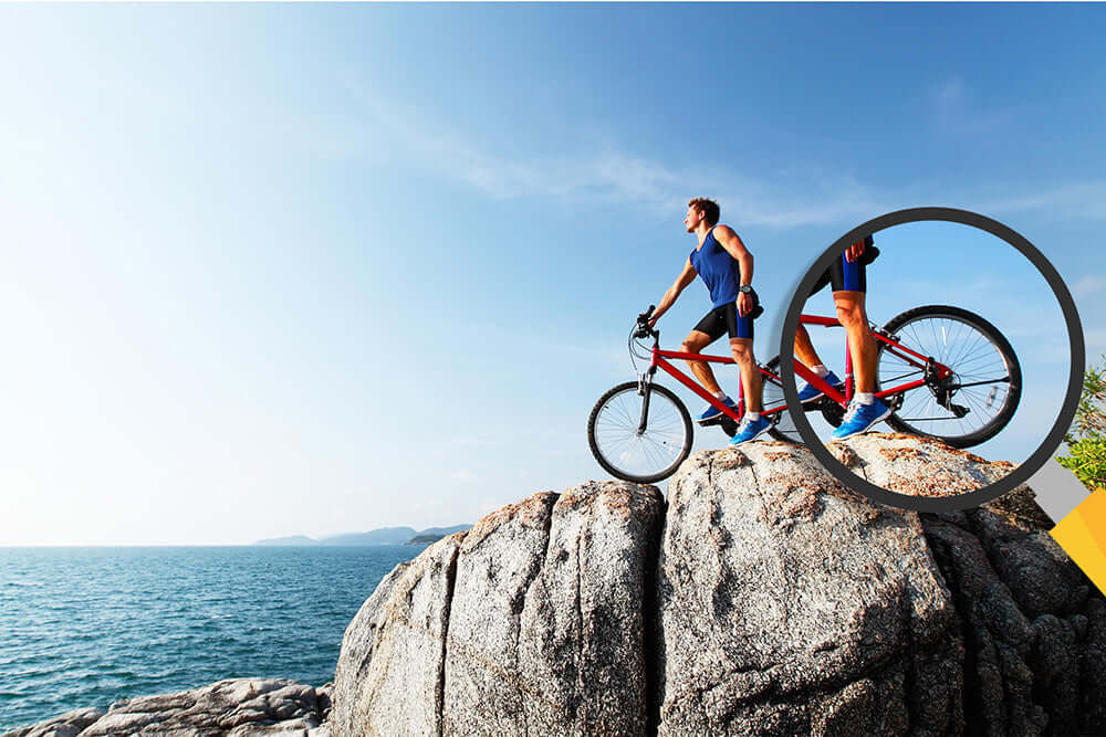 A man on a red bike standing on a rock near the sea, enjoying a scenic view outdoors.